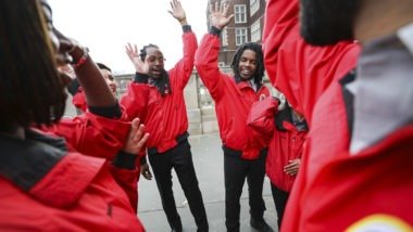 A team of City Year AmeriCorps members raise their hands at the end of a team huddle